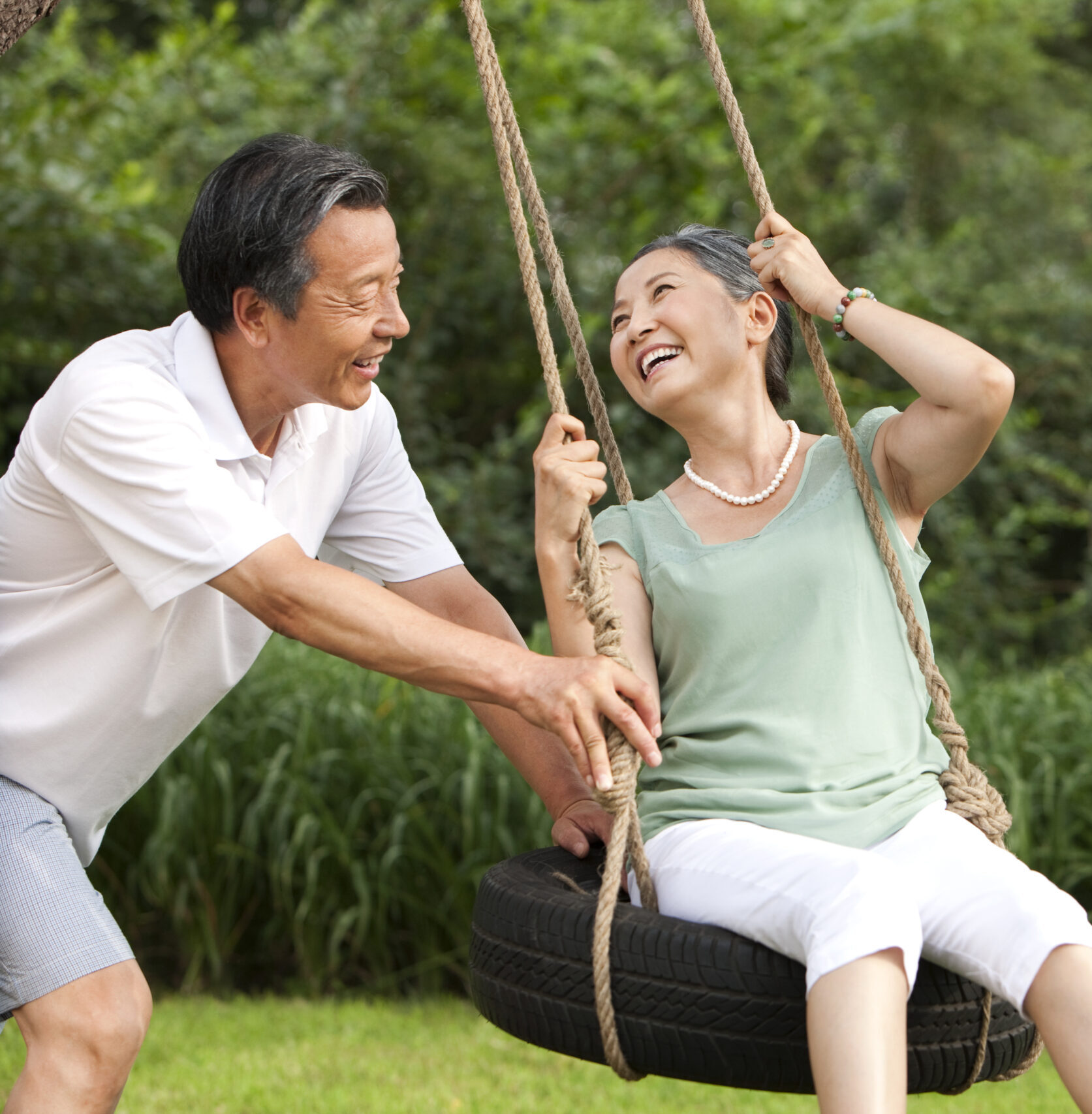 Cheerful senior Chinese couple playing on a swing