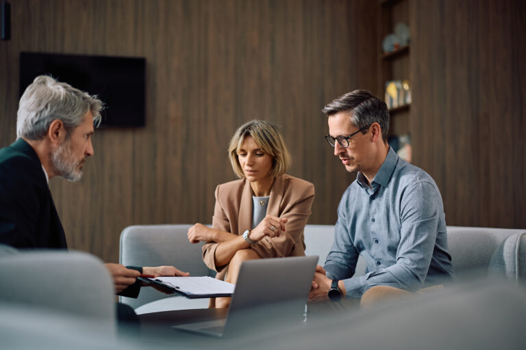 An adviser talking through paperwork with a couple at a table, a laptop and documents in front of them.